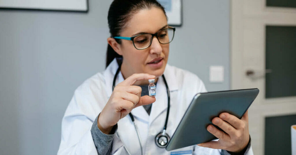 Photo showing a lady doctor with an electronic device apparently giving instructions for digitalisation in healthcare for patient safety.